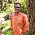 Javier Aztiazarain smiles at the camera while standing among trees in the UC Davis Arboretum. 