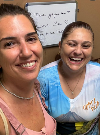 Stephanie Fallas (right) and a student (left) taking a selfie indoors with a whiteboard displaying thank you messages behind them.