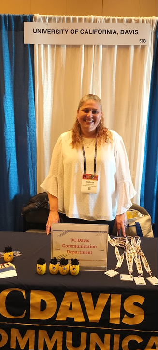 Stephanie Fallas standing behind a UC Davis communications booth at 2024 NCA recruitment event.