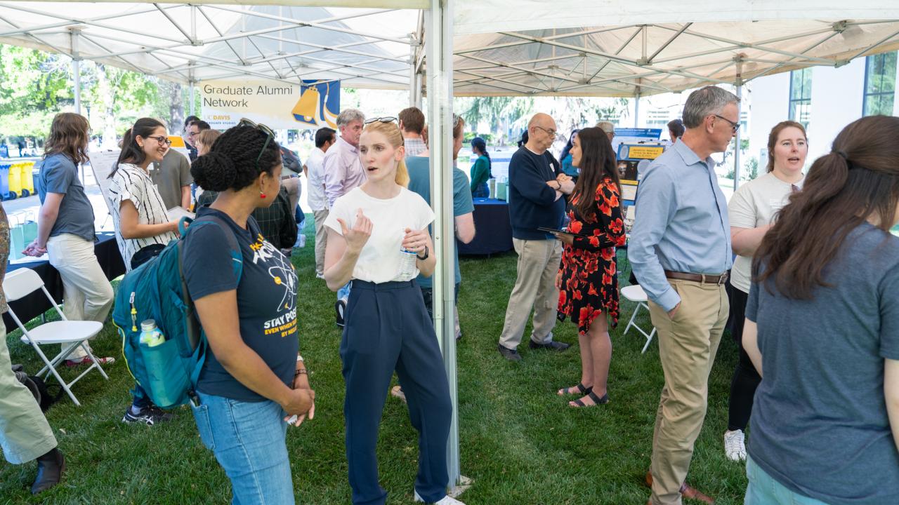 Wide shot of the exhibition tent, showing students presenting their research and mingling with alumni, faculty and staff, with the Graduate Alumni Network banner in the background.