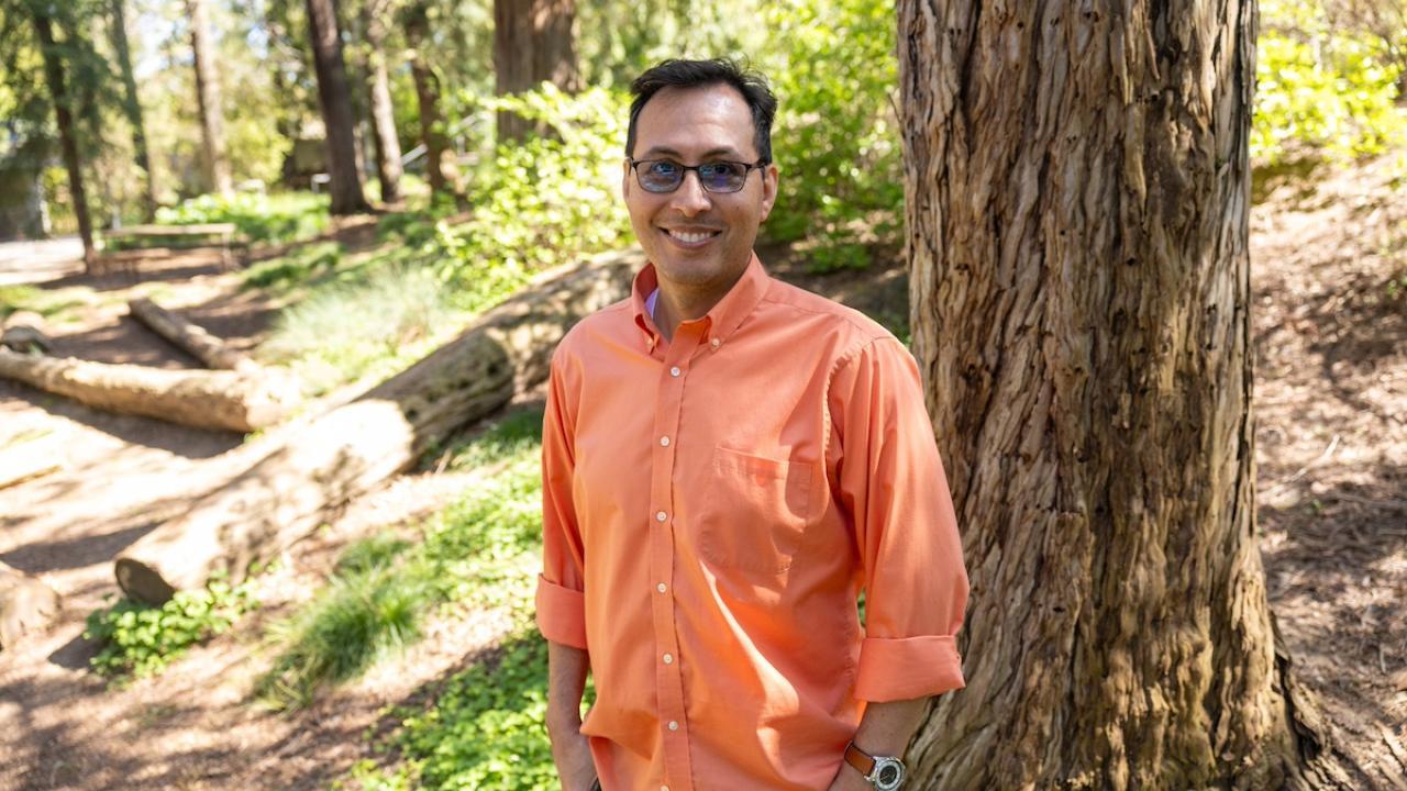 Javier Aztiazarain smiles at the camera while standing among trees in the UC Davis Arboretum. 