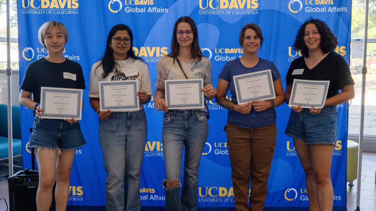 Five students holding certificates stand in front of a UC Davis Global Affairs backdrop.