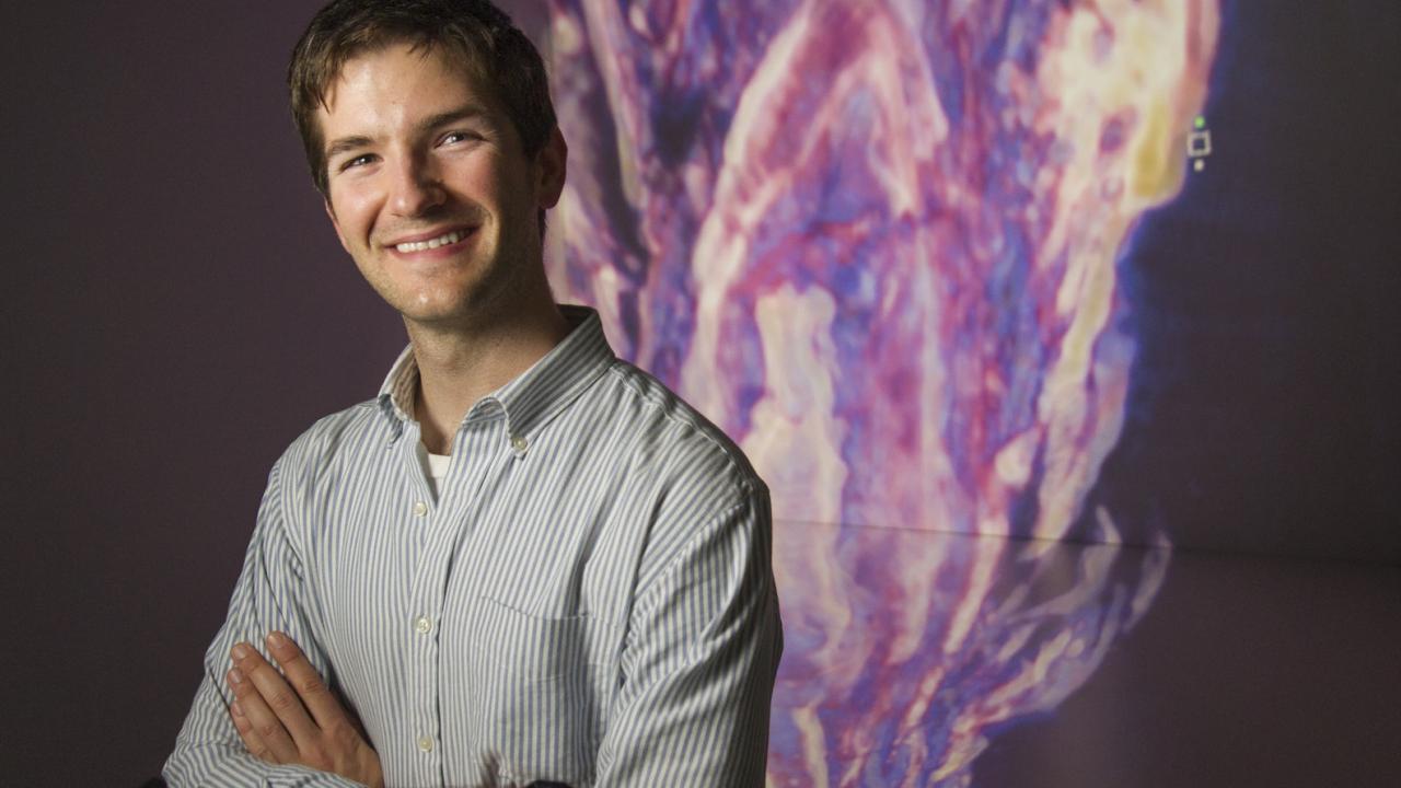 Tyler Mackey in front of a 3D projection of structures built by microbes