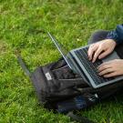 Student types on a laptop while sitting on green grass
