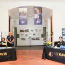 Smiling staff at two UC Davis Graduate Studies information tables in Walker Hall North Lobby with 100th Anniversary banners hanging above them.