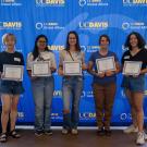 Five students holding certificates stand in front of a UC Davis Global Affairs backdrop.
