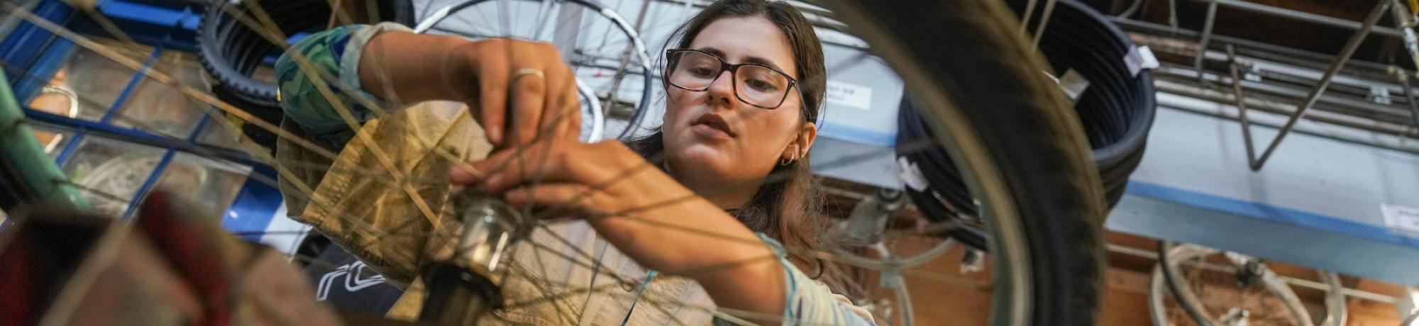 Student wearing glasses uses a tool to fix a bike wheel in the Bike Barn