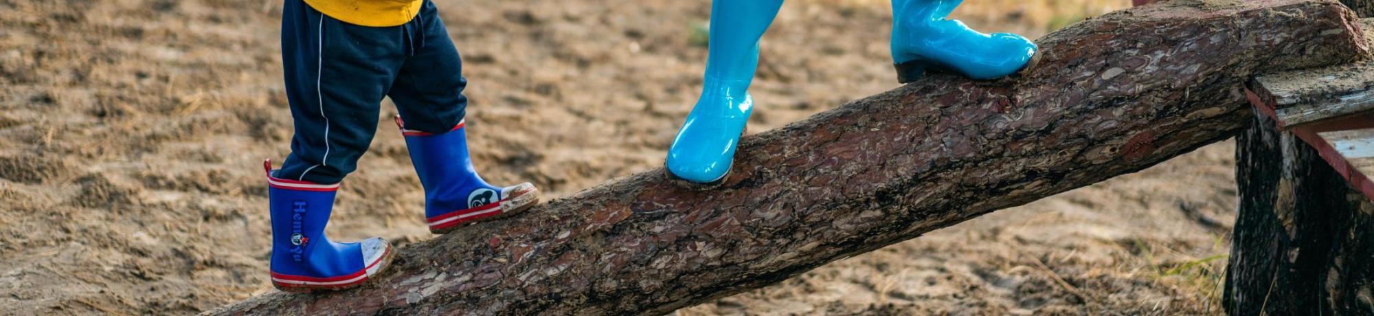 Parent in blue jeans helping small child climb log